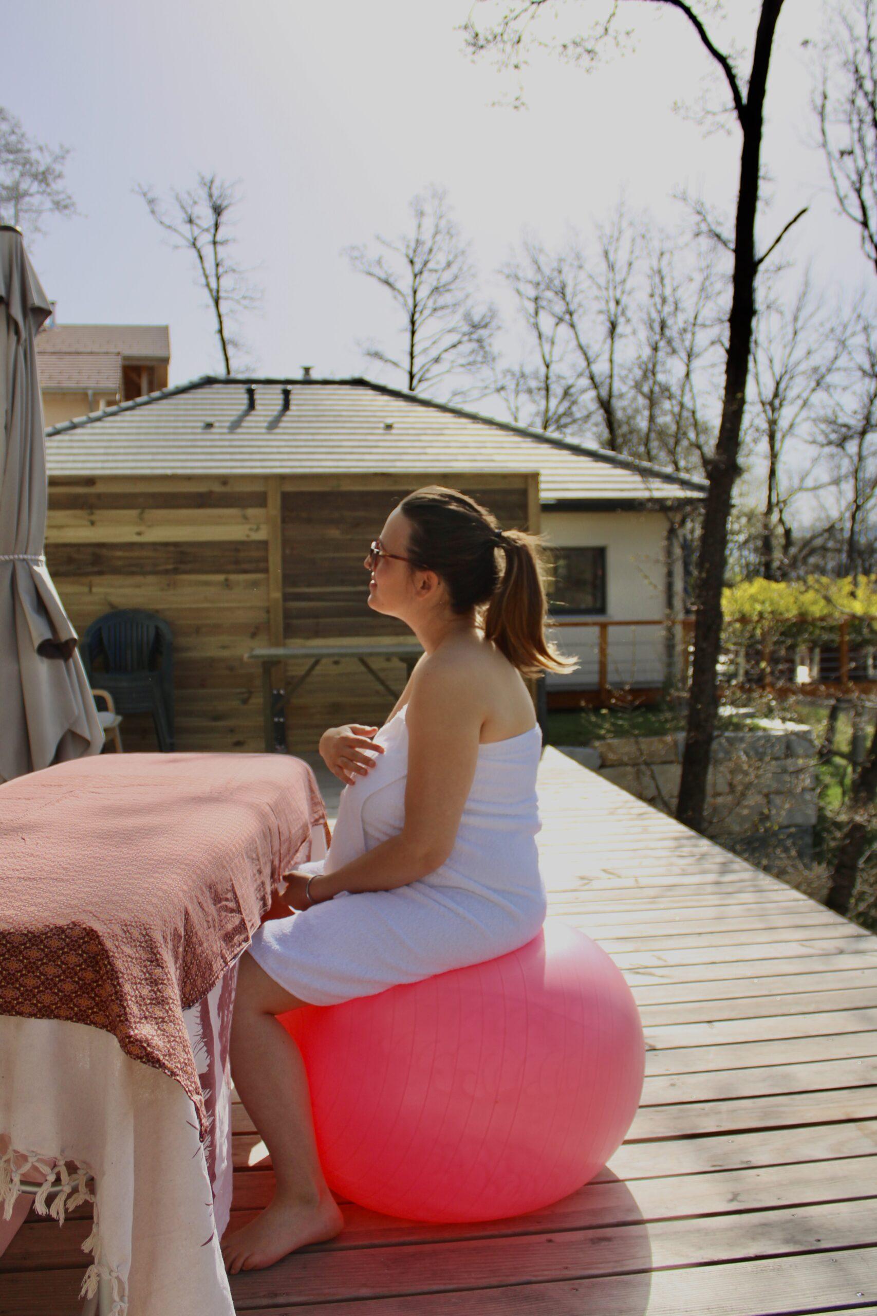 Future maman assise sur un ballon à côté d’une table de massage